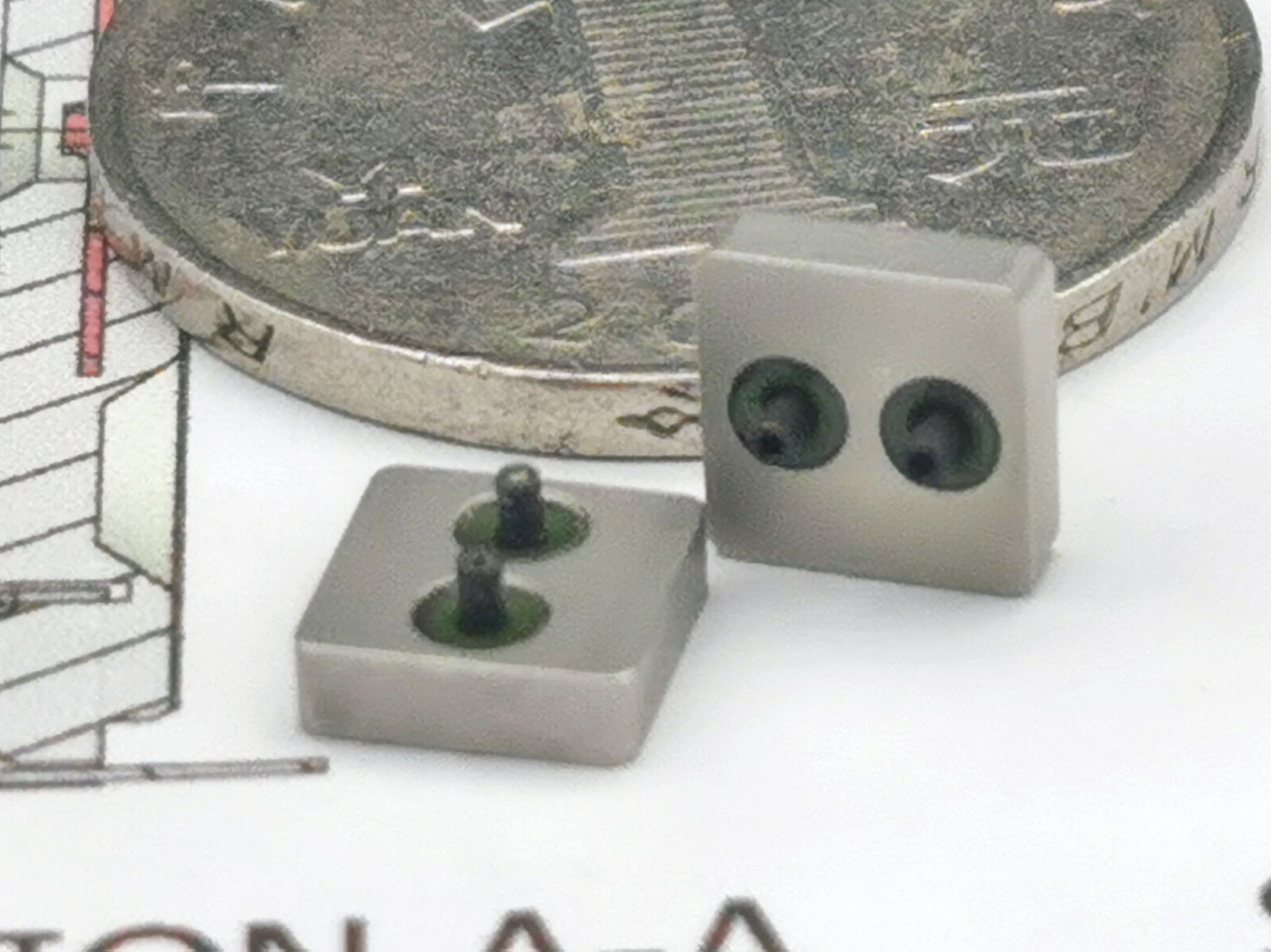 Close-up of small electronic components next to a coin on a technical drawing background.